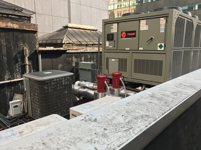 A rooftop with industrial HVAC units, including a large Trane chiller, various ducts, and smaller equipment.