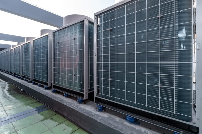 A row of large commercial HVAC systems lined up on a rooftop under a clear sky.