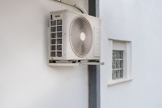 An air conditioner is hanging on the side of a building.